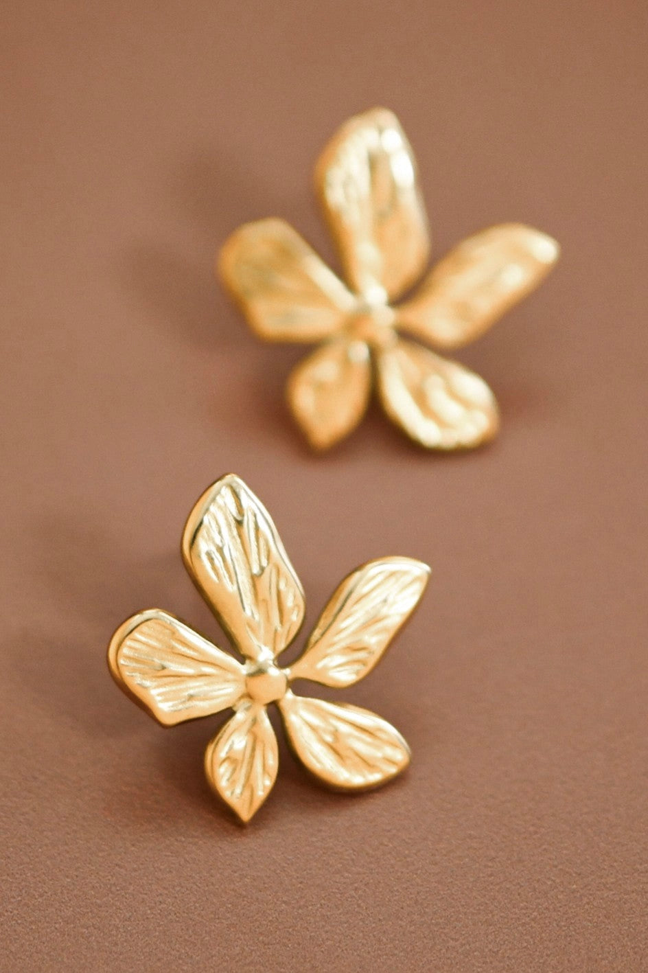 18K gold plated stainless steel blooming flower stud earrings held between fingers.