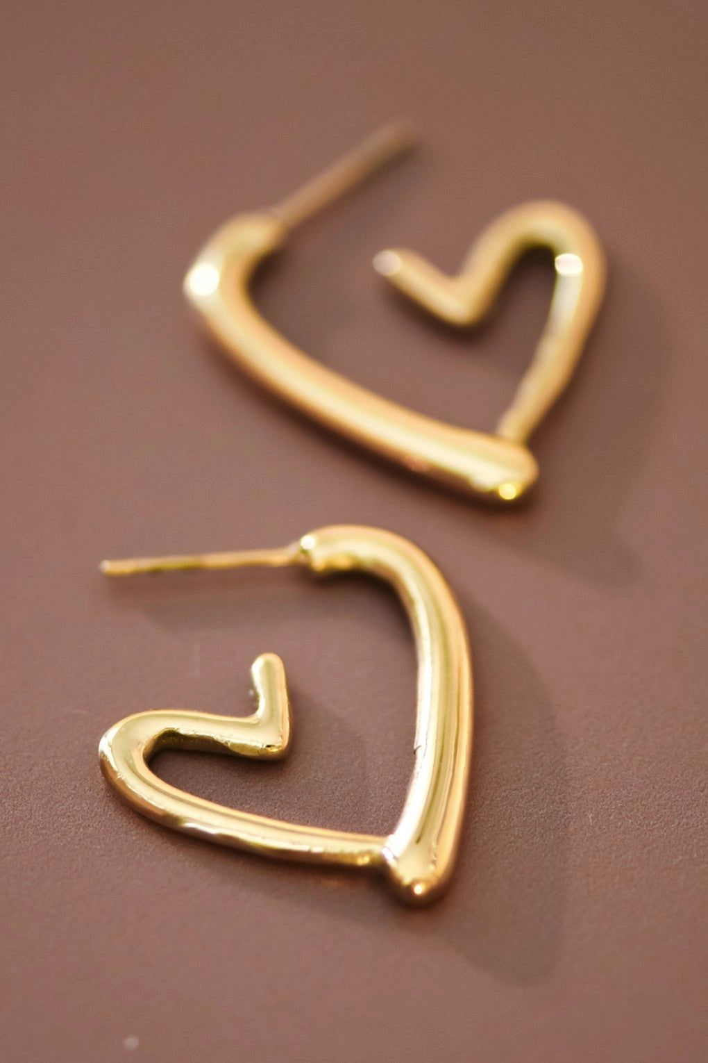 18K gold plated stainless steel chunky heart-shaped hoop earrings held between fingers.