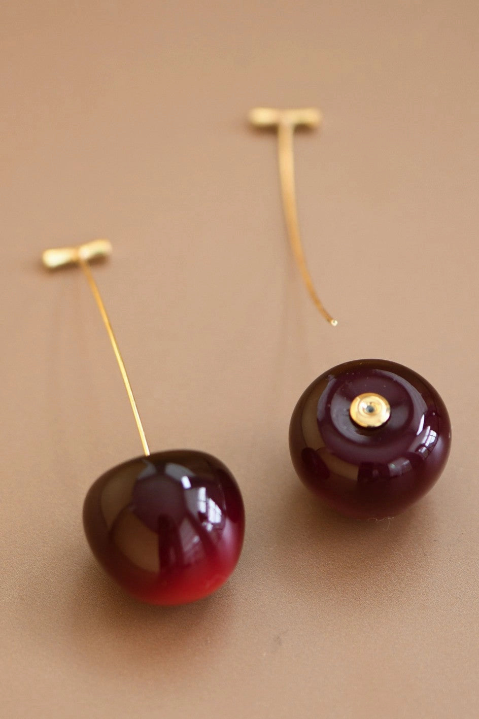 Hand holding a pair of cute 3D red cherry threader earrings for jewelry detail