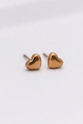 Tiny 18K gold plated heart stud earrings shown on a fingertip to highlight their dainty 0.25 inch size.