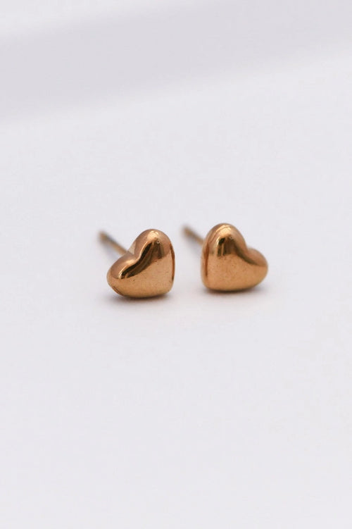 Tiny 18K gold plated heart stud earrings shown on a fingertip to highlight their dainty 0.25 inch size.