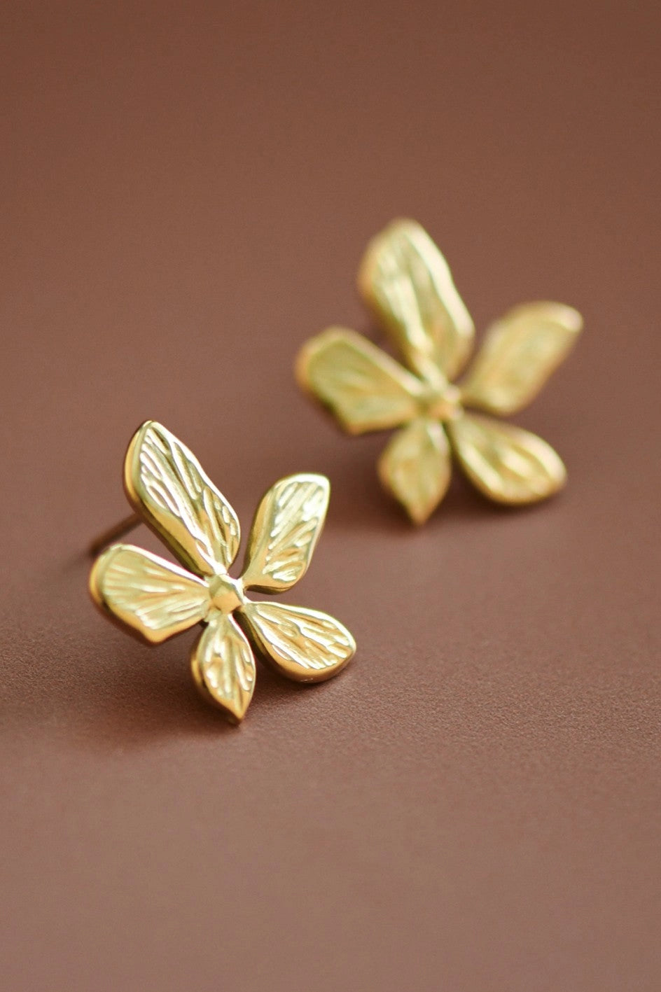 Modern 18K gold flower stud earrings worn on the ear, showcasing their artistic botanical design.