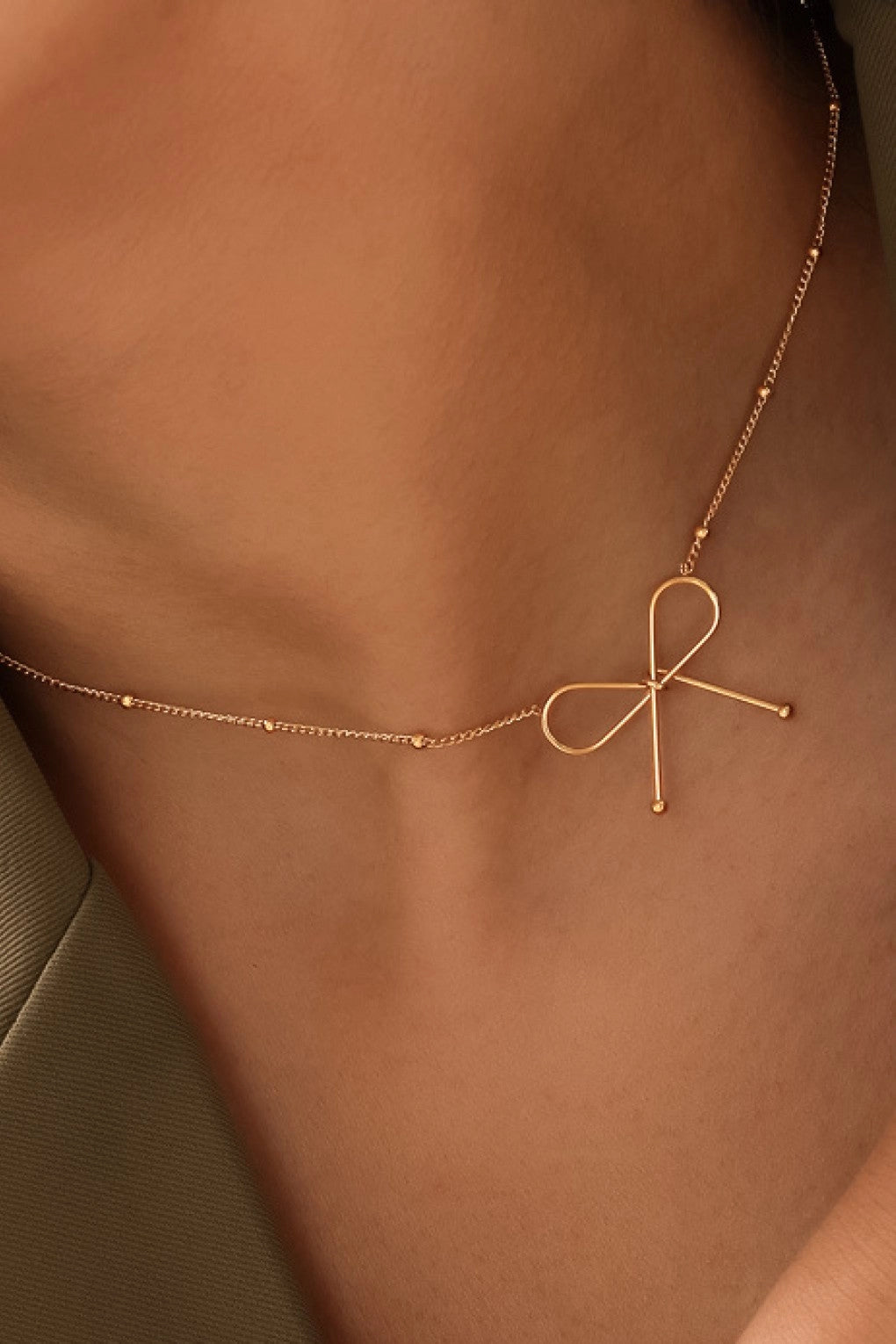 Dainty gold chain necklace with a bow pendant resting on a hand, showing its rich 18K gold finish.