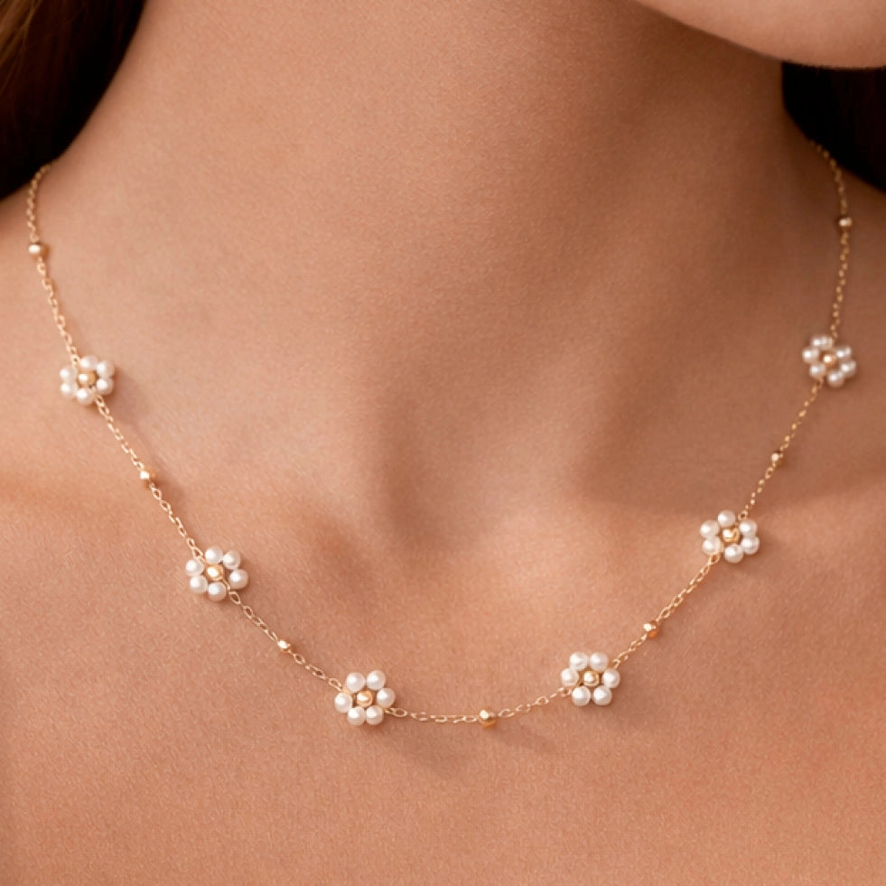 Dainty gold chain necklace with flower bead charms resting on a hand, showing the rich 18K gold tone.