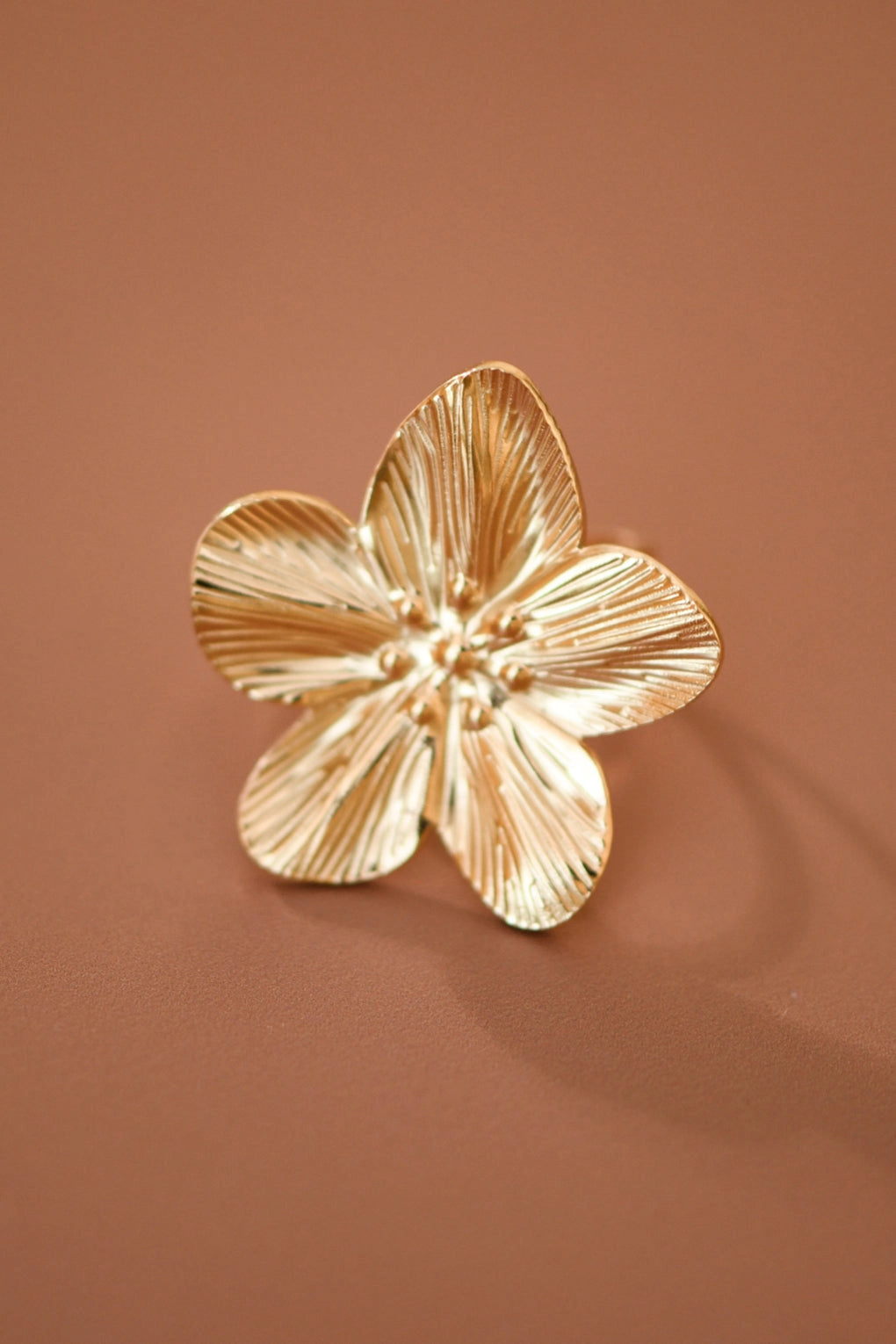 Detailed view of adjustable gold-plated flower ring worn on finger, highlighting the rich gold tone