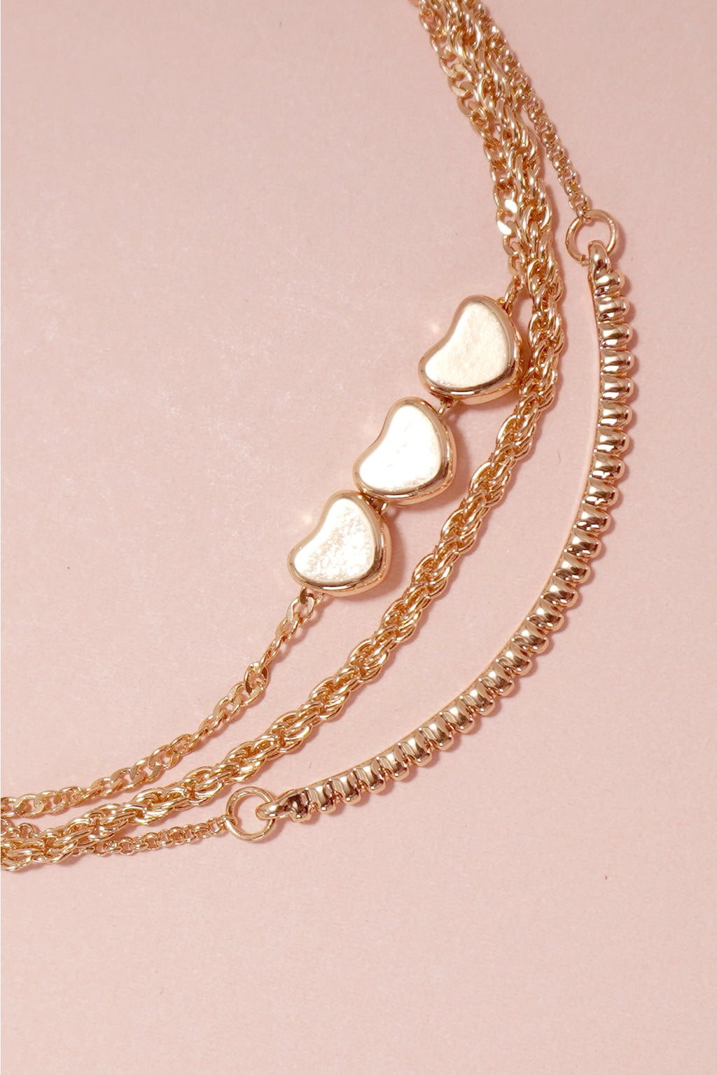 Close-up of the delicate heart charms and different chain textures on the layered gold bracelet.