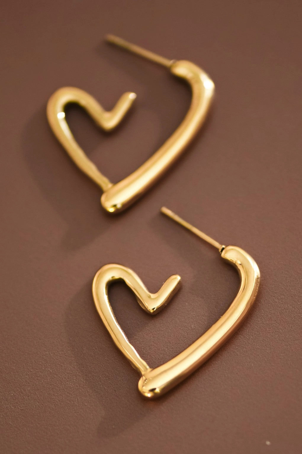 Bold gold heart hoop earring resting on a hand, showcasing the thick design and polished 18K gold finish.
