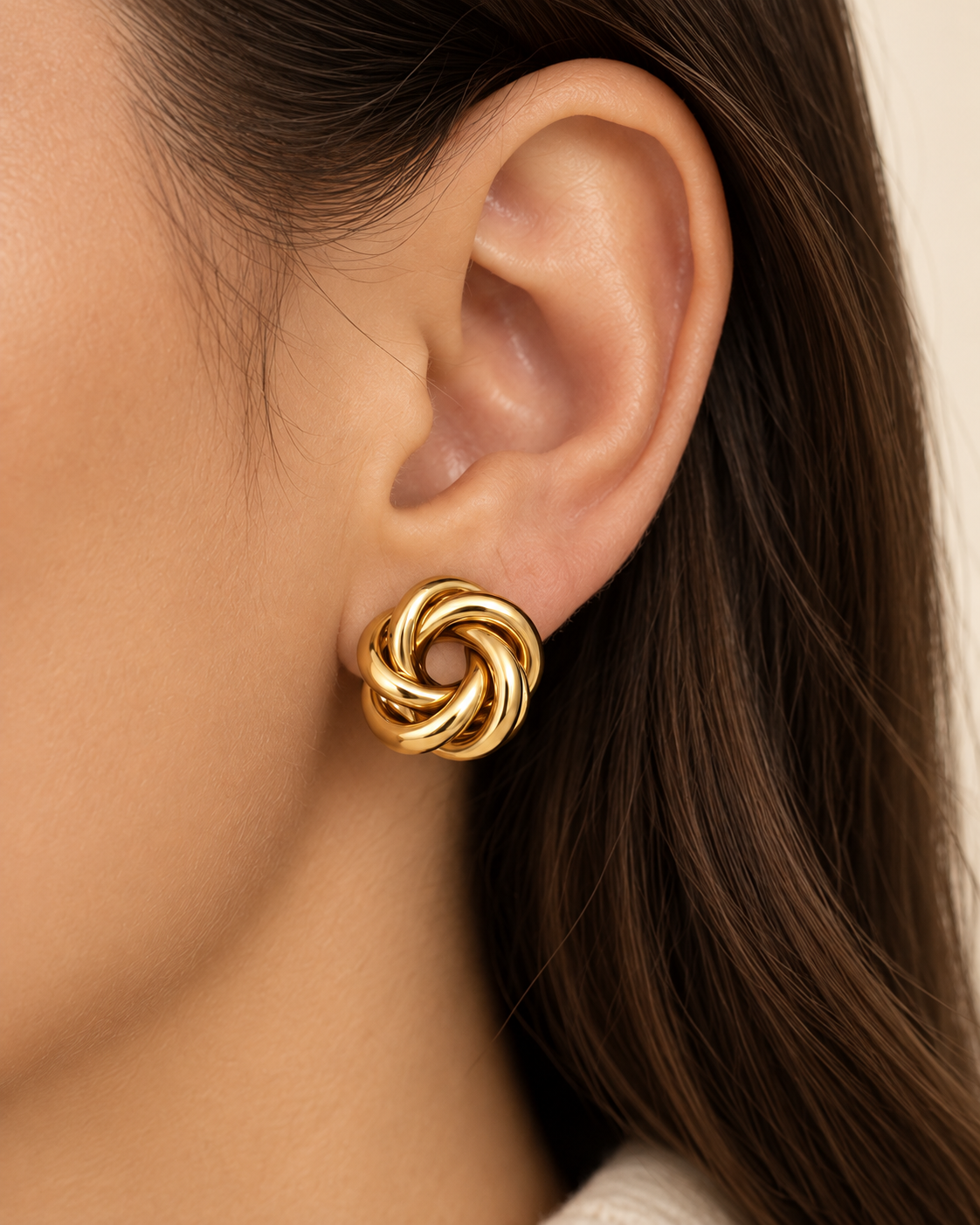 Gold knot stud earrings worn on ear showing statement size and twisted design