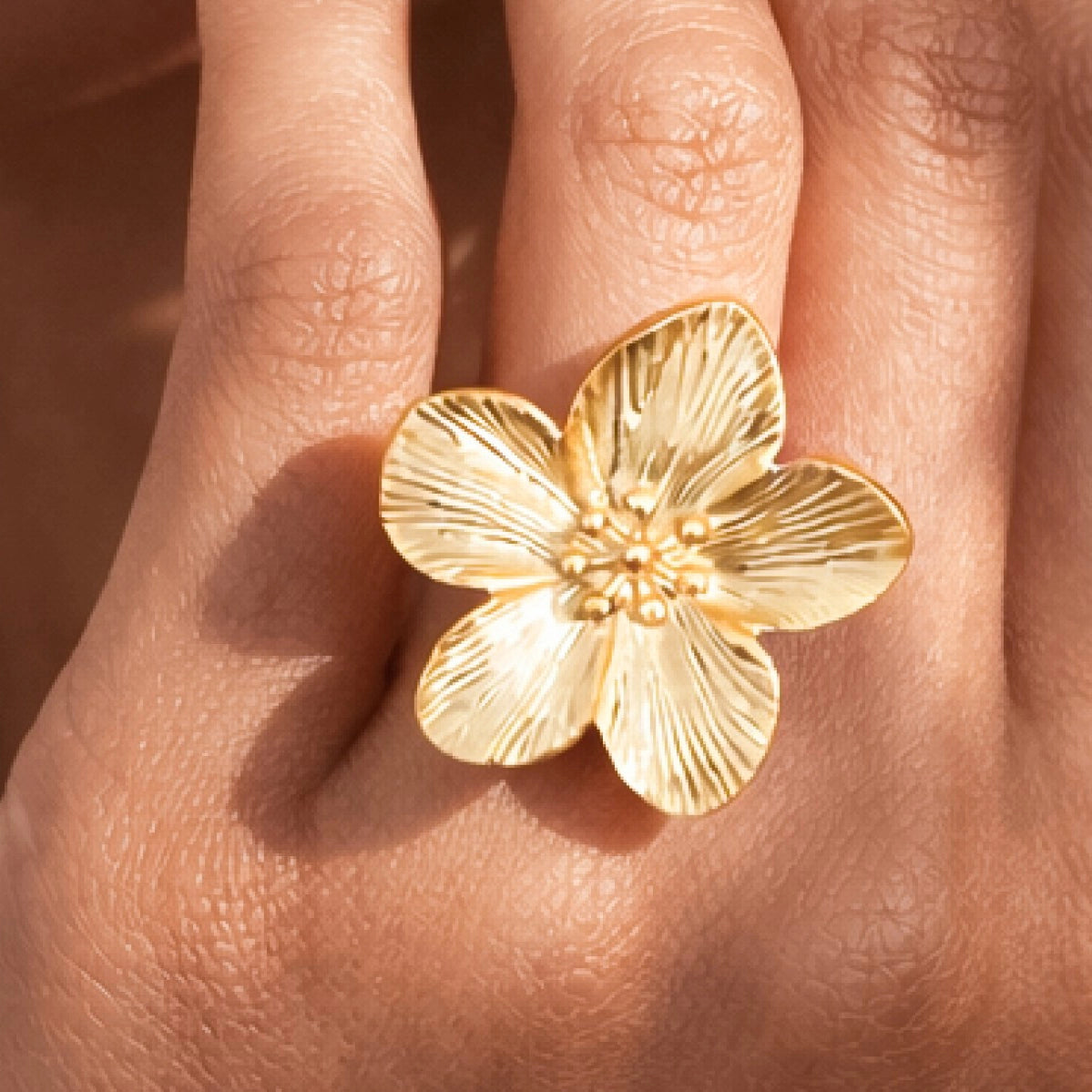 Close-up of 18k gold plated adjustable flower ring being worn on a woman's finger