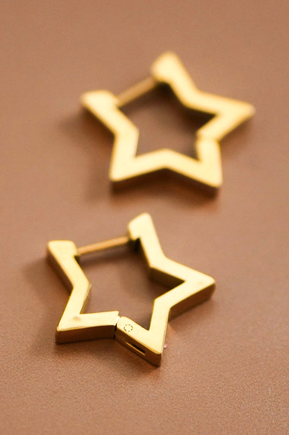 Dainty gold star earrings resting on a hand, showcasing their 0.8 inch size and polished 18K finish.