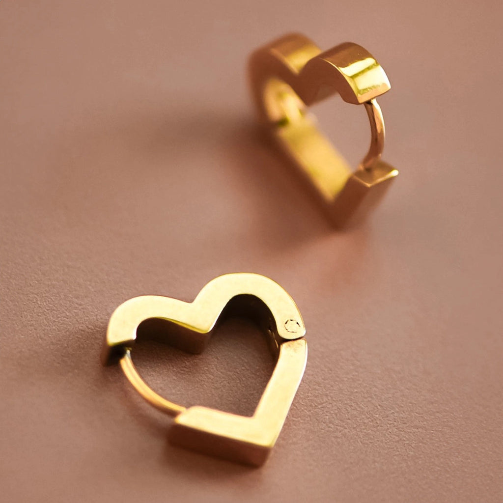 Minimalist 18K gold heart huggie hoops worn on the ear, showing how they sit close to the lobe.