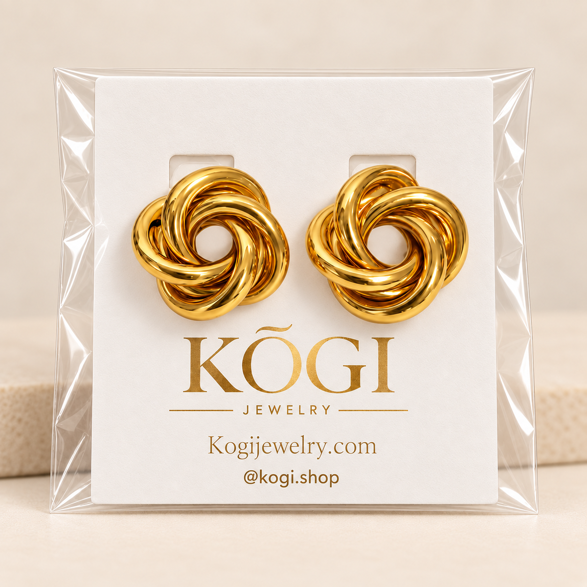 KOGI gold knot stud earrings displayed on branded jewelry packaging