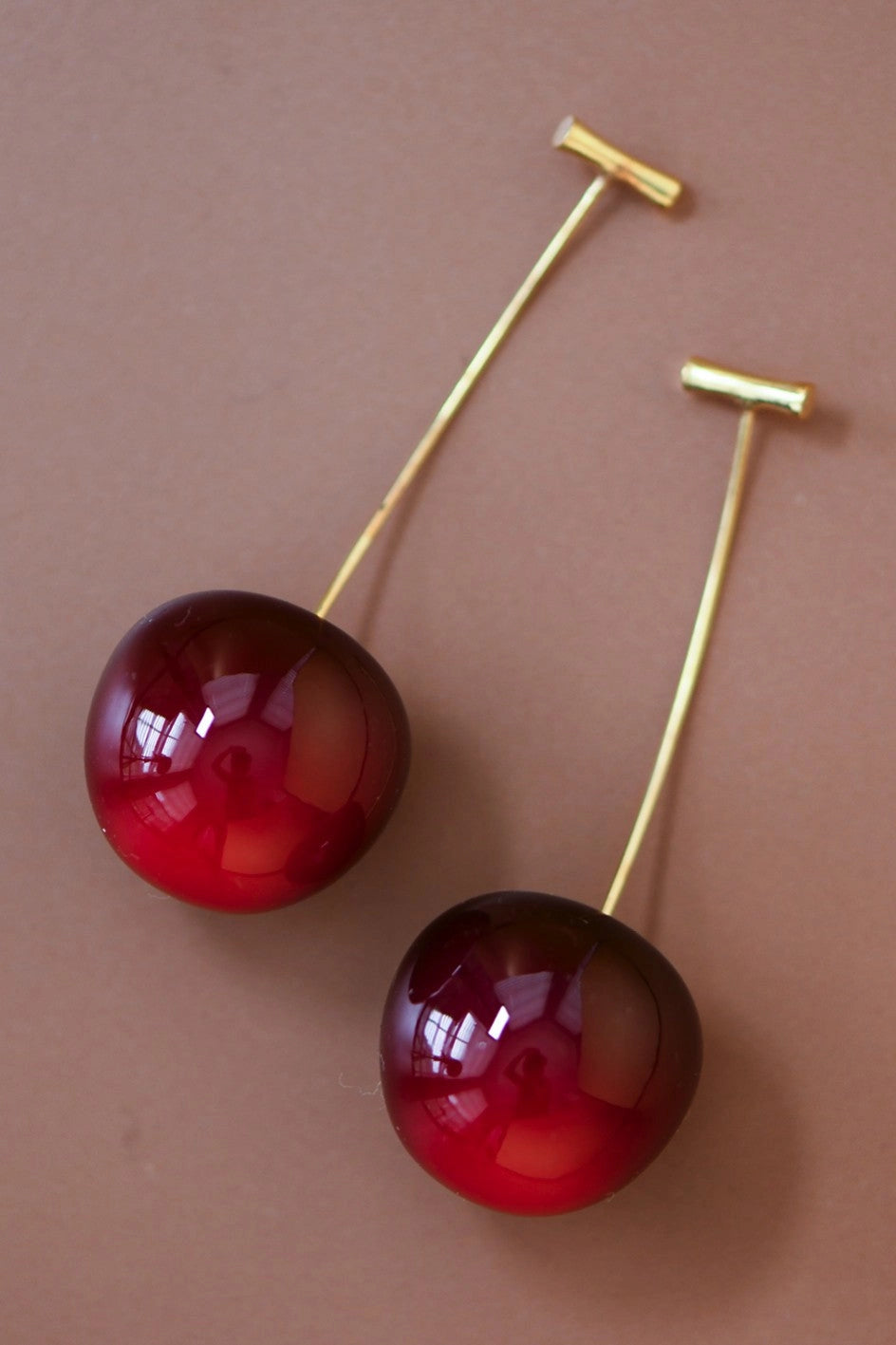 Pair of 3D red cherry dangle earrings on a brown background by Kogi Jewelry