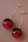 Pair of 3D red cherry dangle earrings on a brown background by Kogi Jewelry