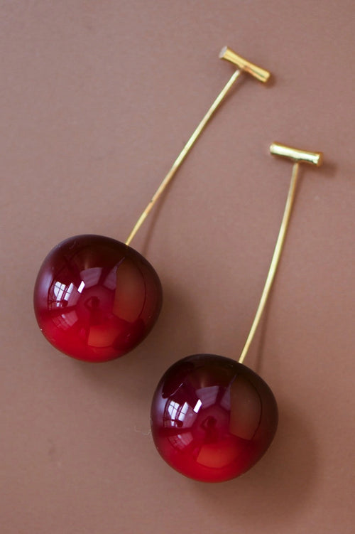 Pair of 3D red cherry dangle earrings on a brown background by Kogi Jewelry