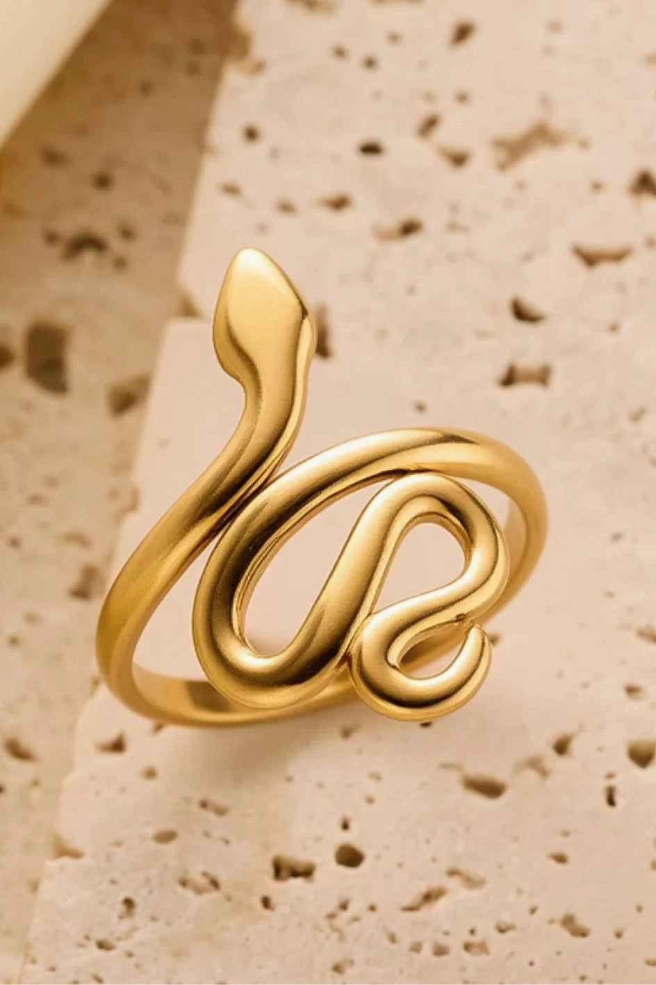 Aesthetic view of the 18K gold snake wrap ring on a stone background, highlighting its rich golden tone.