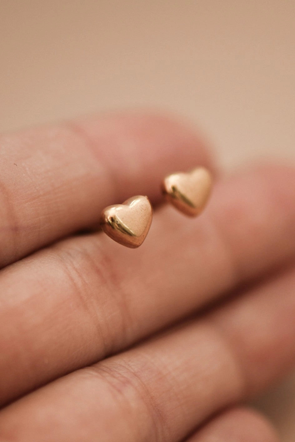 Pair of minimalist gold heart studs on a hand, showcasing the polished 18K gold finish.