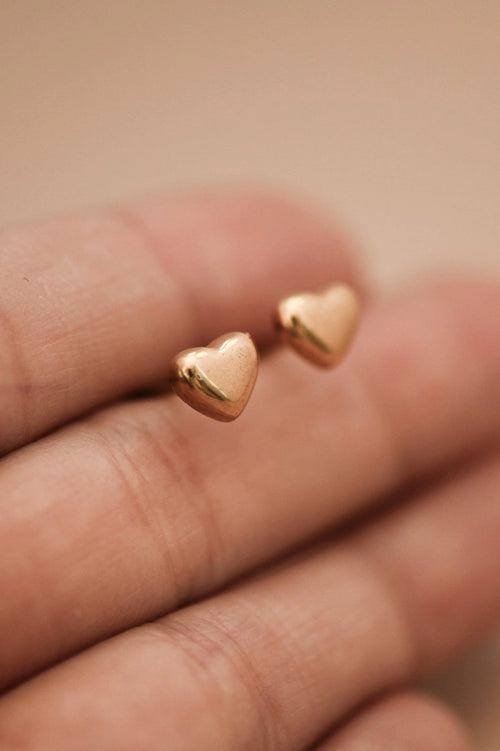 Pair of minimalist gold heart studs on a hand, showcasing the polished 18K gold finish.