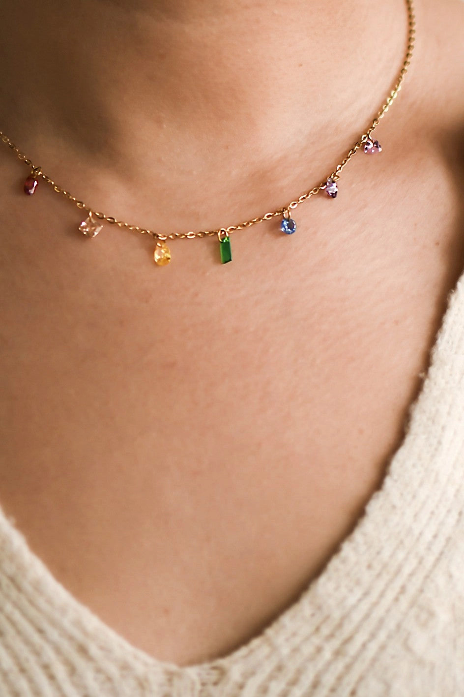 A delicate 18K gold plated chain necklace with multi-colored crystals rests on a woman's hand, showing the tarnish-resistant finish.