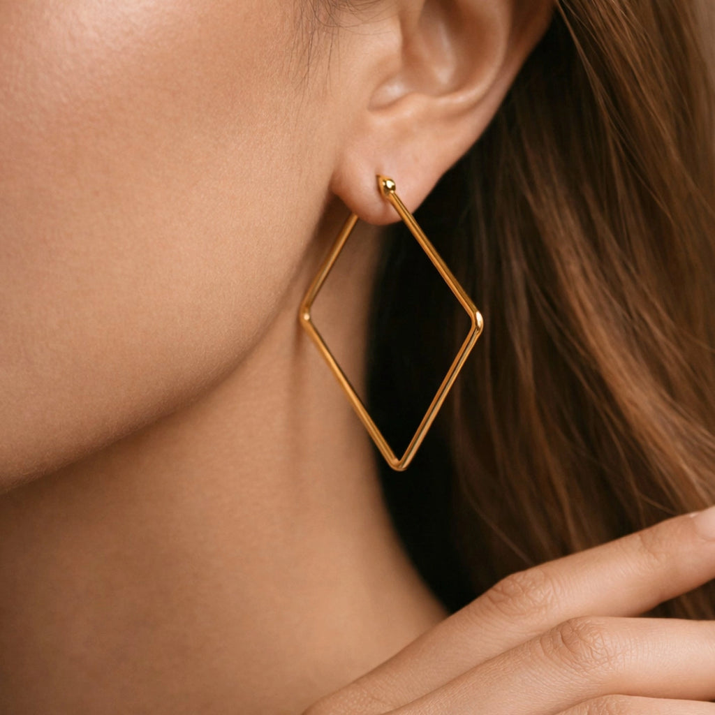 Large 18K gold plated stainless steel square hoop earrings held between fingers by Kogi Jewelry.