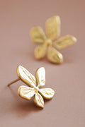 Pair of sculpted gold flower studs on a hand, showing the organic petal details and 0.7 inch size.