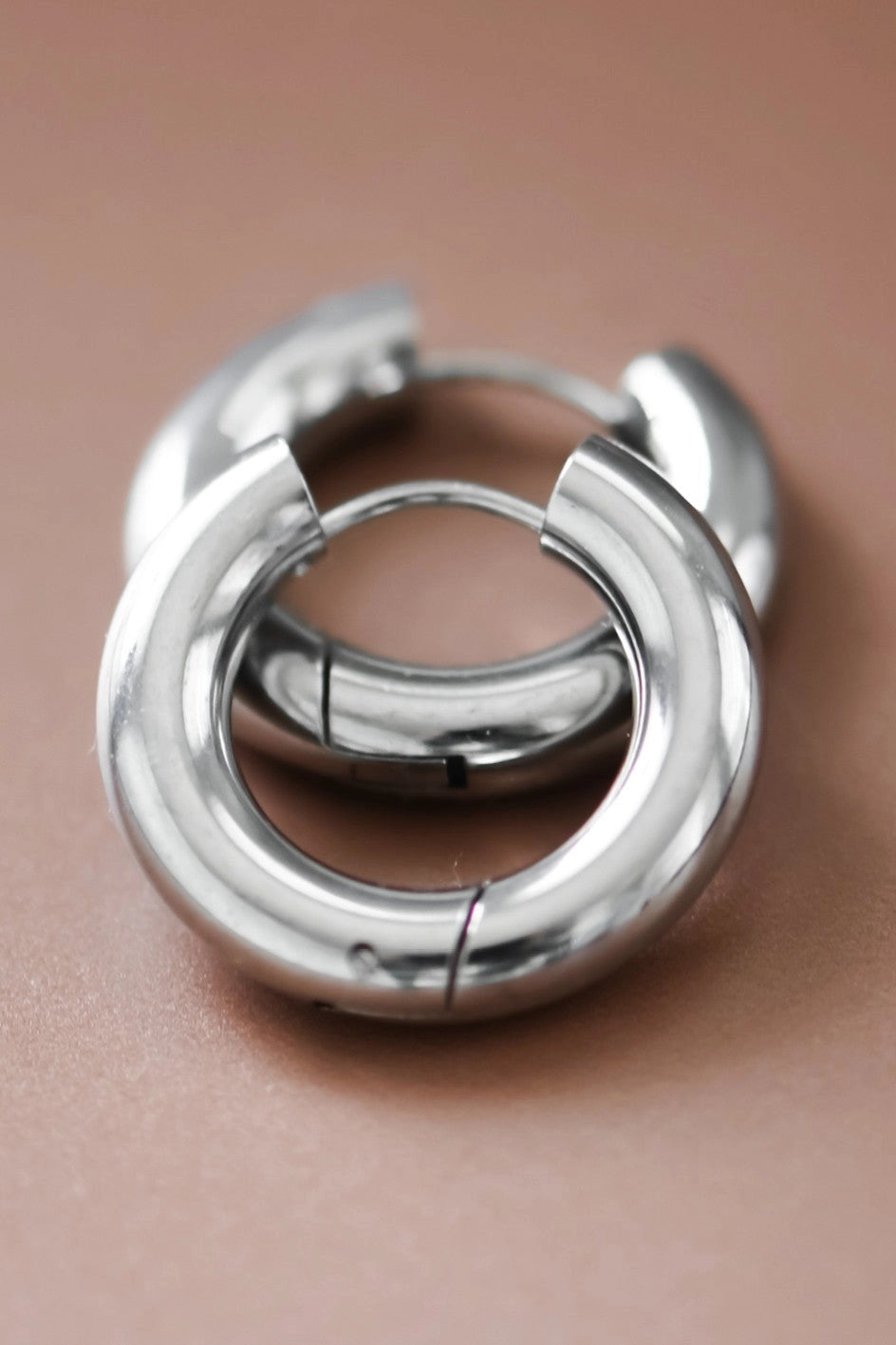 High-shine silver chunky hoop earrings in polished stainless steel held between fingers.