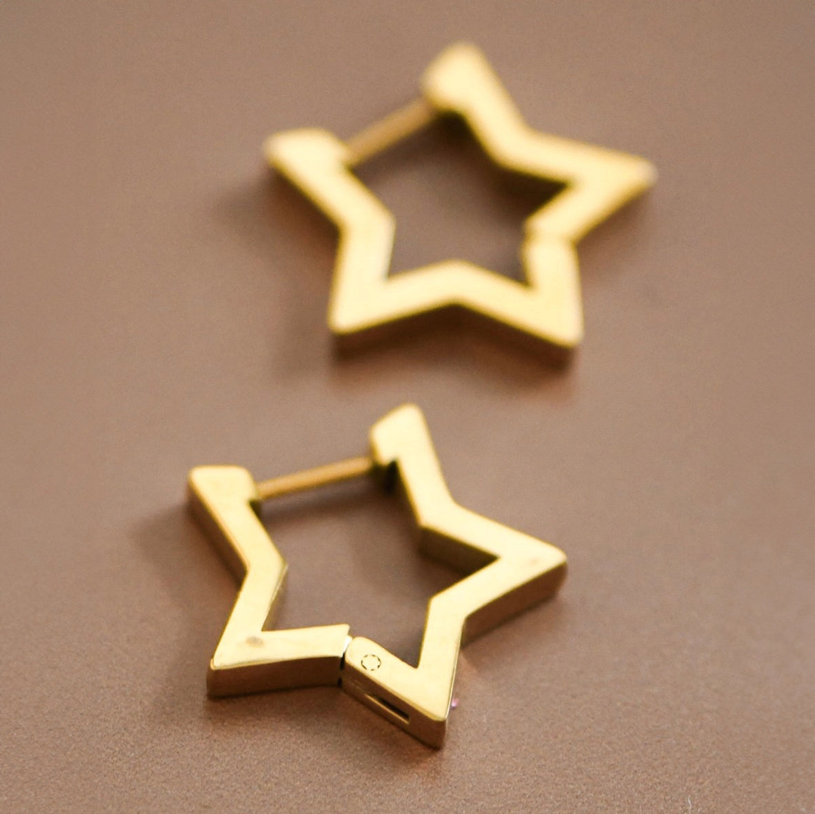 18K gold plated stainless steel star-shaped huggie earrings held between fingers by Kogi Jewelry.