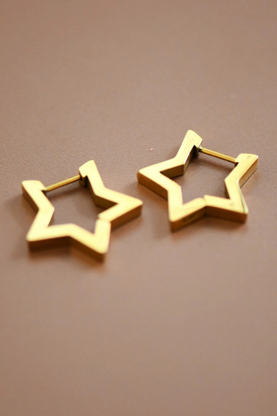 Minimalist 18K gold star huggie hoops worn on the ear, highlighting their geometric celestial design.