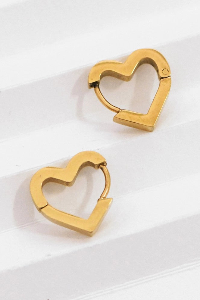 Pair of tarnish-free 18K gold plated heart earrings on a hand, highlighting the rich golden color.