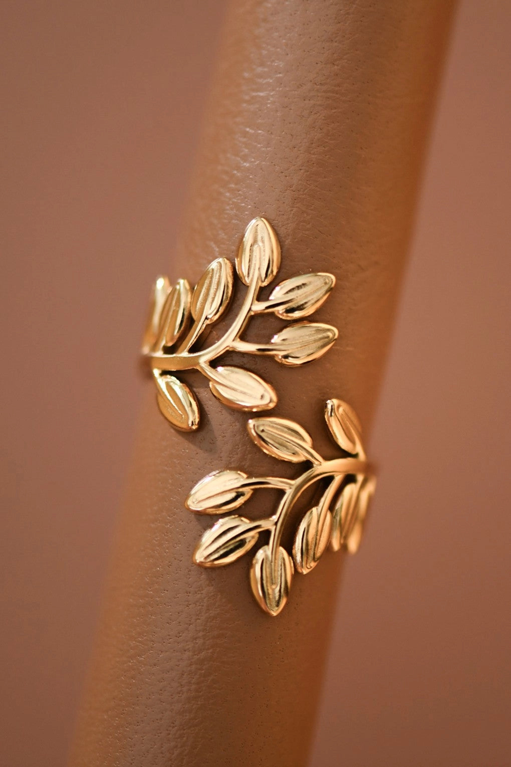 Waterproof gold leaf branch ring on a neutral stone background, reflecting a rich 18K gold tone.
