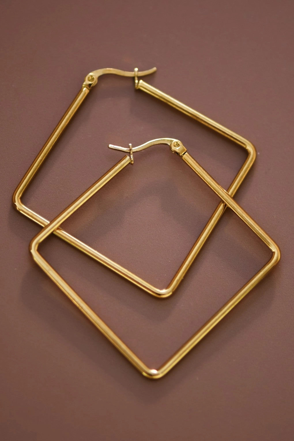 Pair of tarnish-free 18K gold plated large square earrings on a hand, showcasing the rich golden color.