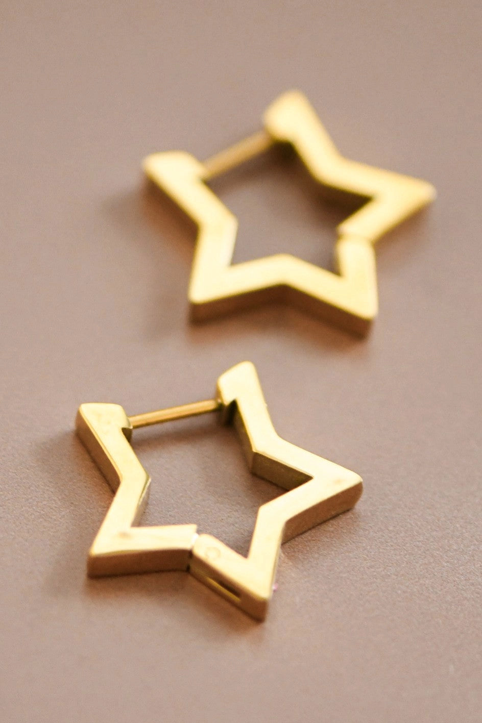 Pair of tarnish-free 18K gold plated star earrings on a hand, showing the rich golden color.
